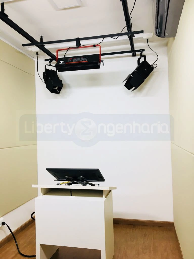 Sala de gravação com equipamentos de iluminação no teto e uma mesa para a televisão