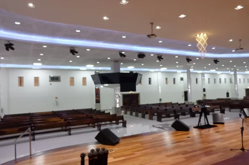 Salão principal de Igreja bem iluminado com bancos e vazios visto do palco