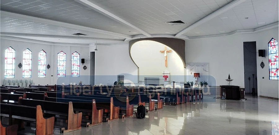 Salão principal de igreja com bancos de madeira dispostos e crucifixo acima do púlpito