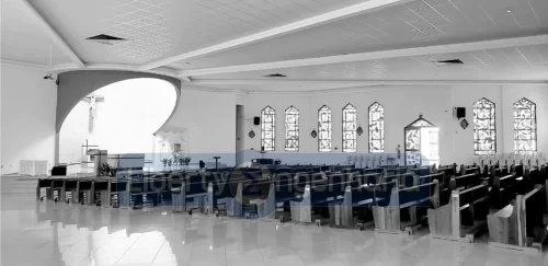 Imagem em preto e branco de salão principal de igreja com bancos de madeira e vitrais nas paredes
