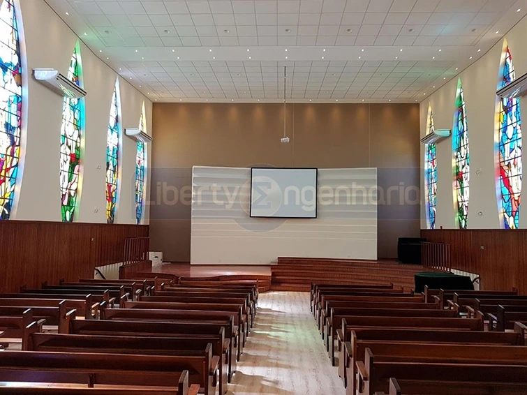 Púlpito com televisão e bancos de madeiras dispostos no salão principal de igreja com vitrais coloridos