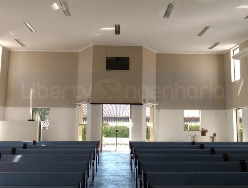 Salão principal de igreja com televisão e bancos pretos para o público com porta dupla de vidro para saída