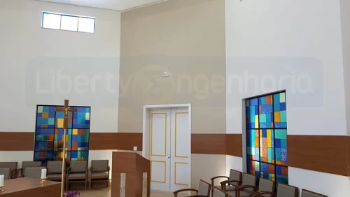 Púlpito em frente à porta branca e vitrais coloridos em capela revestida com painel acústico