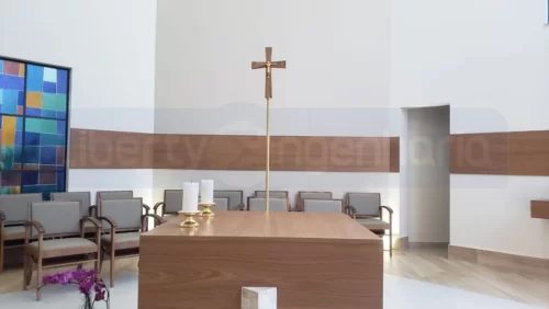 Decoração de cruz e pequenas velas em cima de mesa em capela revestida com painéis acústicos